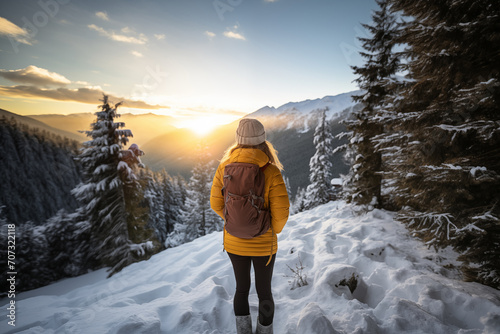 Generative AI back view image of an unrecognizable woman in a yellow jacket standing and observing a sunset in a snowy mountain landscape photo