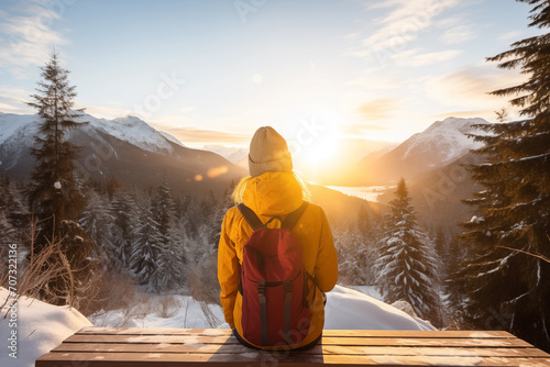 Generative AI back view image of an unrecognizable woman in a yellow jacket sitting and observing a sunset in a snowy mountain landscape photo
