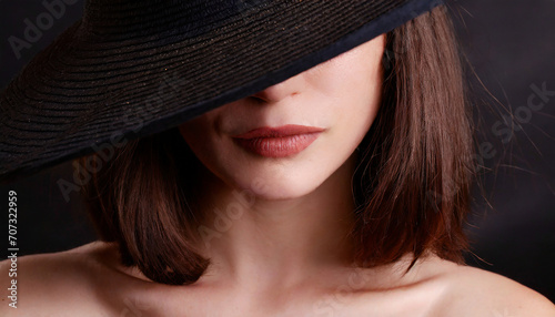 Portrait of young woman with face partly hidden by elegant hat 