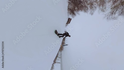 A snowboarder films himself on a 360 camera, snowboarding, ski resort, snowboarder in motion, snowboarder in black clothes, vertical shooting of a snowboarder, vertical shooting photo