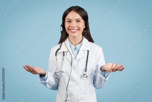Smiling woman doctor with headset gesturing on blue