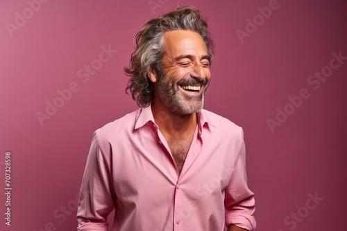 Portrait of a happy senior man laughing against a pink background.