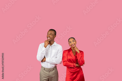 Thoughtful black couple with hand on chins looking up at free space, pink backdrop