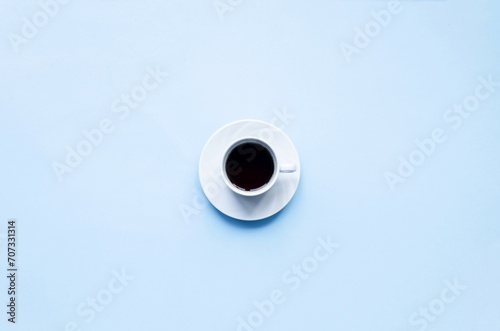 Cup of coffee on a blue background. Delicate, tasty, aromatic black coffee in a small white cup on a white saucer, space for copy text, flat lay, top view.