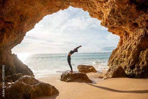 Fit, sporty woman doing a backbend exercise by the sea in a cave