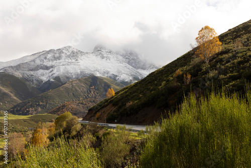 Landscape of road through Las Ubinas natural park with snowy mountains and autumn trees next to green meadow