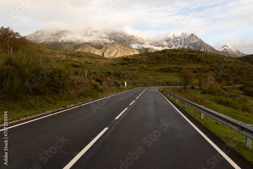 Landscape of road through Las Ubinas natural park with snowy mountains and autumn trees next to green meadow
