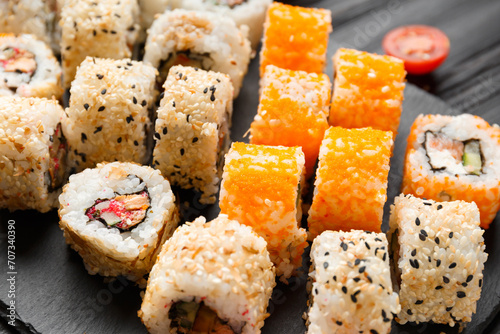 Set of various sushi rolls on a black slate plate, close-up.