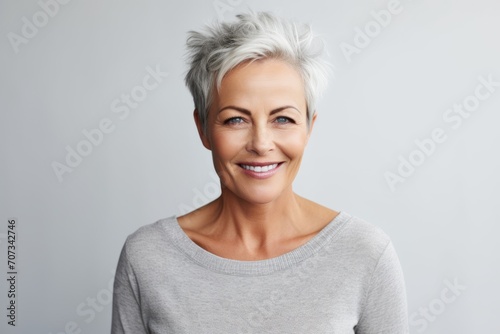 Portrait of a happy mature woman with grey hair standing against grey background photo