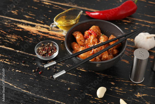 Tasty sweet and sour chicken in bowl with spices on dark wooden background photo