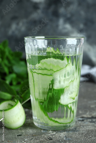 Glass of infused water with cucumber slices on grey table