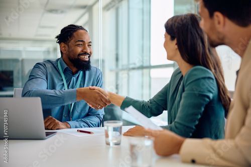 Happy black financial advisor handshaking with his clients during meeting in office. photo