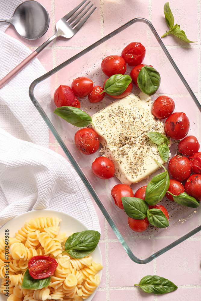 Baking dish with tasty tomatoes, feta cheese and pasta on pink tile background Baking dish with tasty tomatoes, feta cheese and pasta on pink tile background