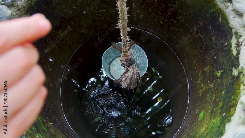 Moneda cayendo a pozo de los deseos hecho de piedra, con cubeta y lazo para sacar agua potable.