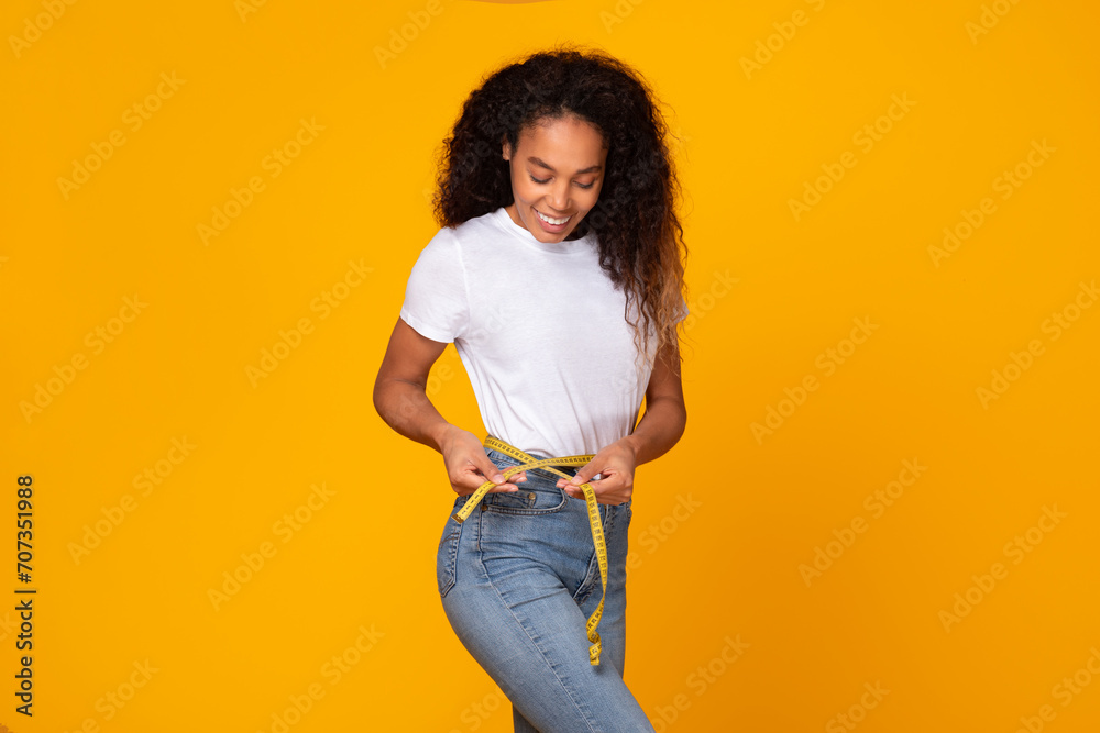 Φωτογραφία African American woman measures waist with tape smiling, yellow background