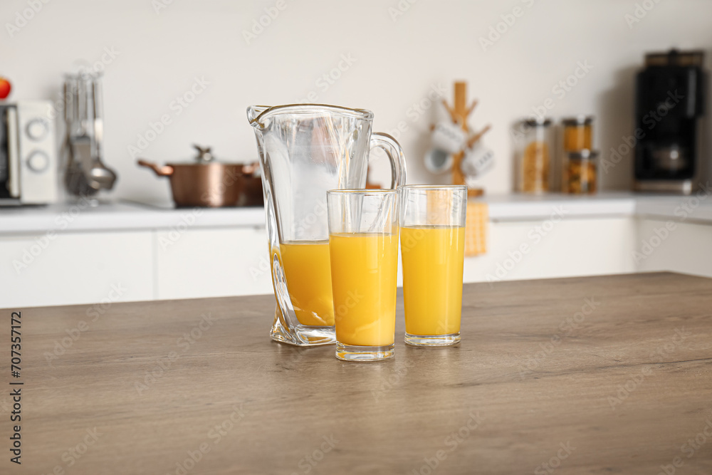 Fototapeta premium Jug and glass of fresh orange juice on table in kitchen
