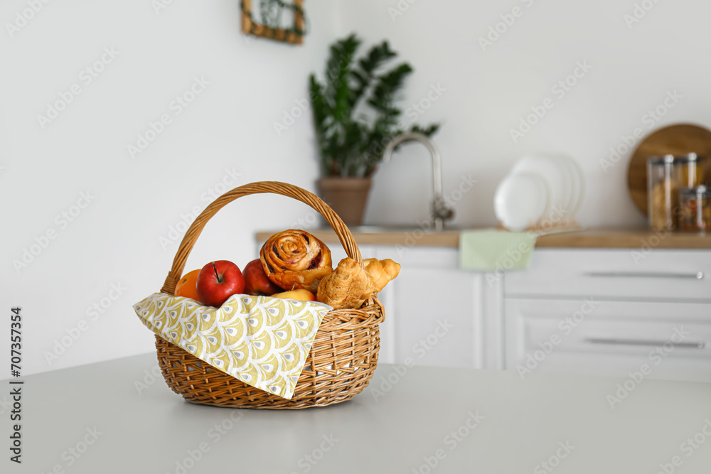 Wicker basket with fruits and fresh pastry on table in kitchen Wicker basket with fruits and fresh pastry on table in kitchen