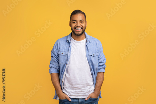 Handsome Black Man With Hands In Pockets Standing On Yellow Studio Background