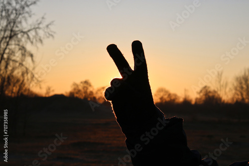 Close-up of a hand in a black knitted glove on the background of a winter sunset with a gesture of victory