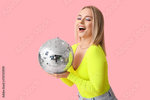 Beautiful young woman with disco ball on pink background