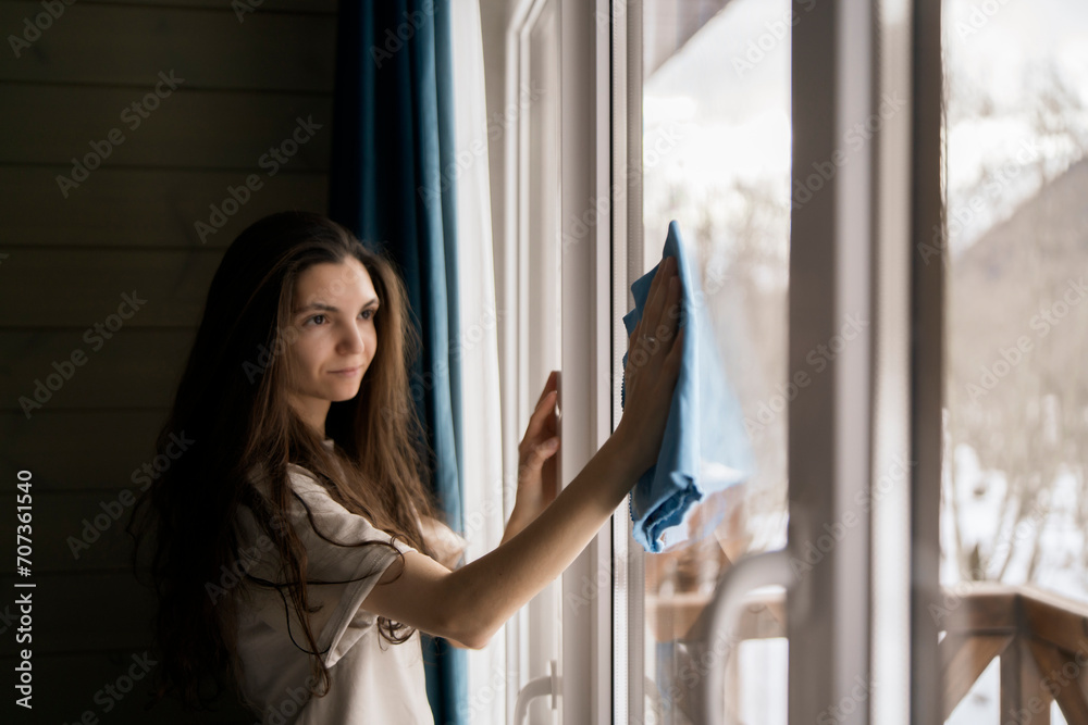 Ταπετσαρία A woman meticulously cleans a windowpane using a blue cloth, with a backdrop of a tranquil, snow-covered environment visible through the glass
