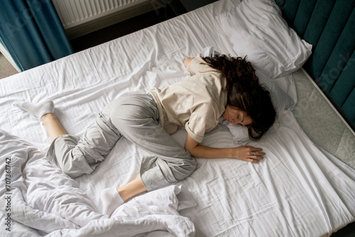 A woman is captured taking a nap, curled up in a bad wrong on a white-sheeted bed, suggesting a midday or early morning rest. photo