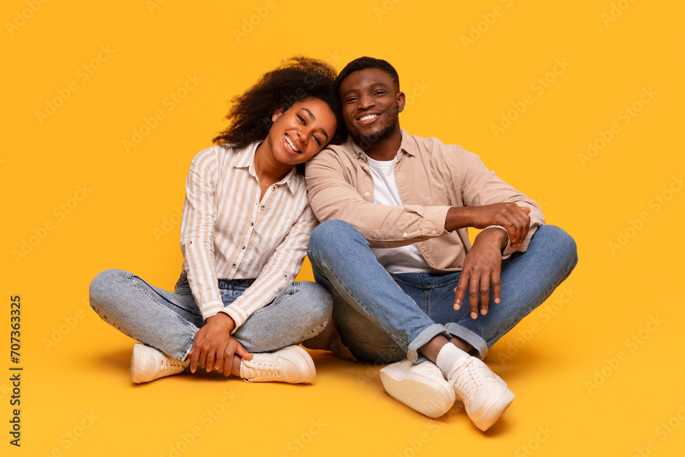 Relaxed black couple sitting together, enjoying cozy moment on yellow background Relaxed black couple sitting together, enjoying cozy moment on yellow background