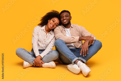 Relaxed black couple sitting together, enjoying cozy moment on yellow background