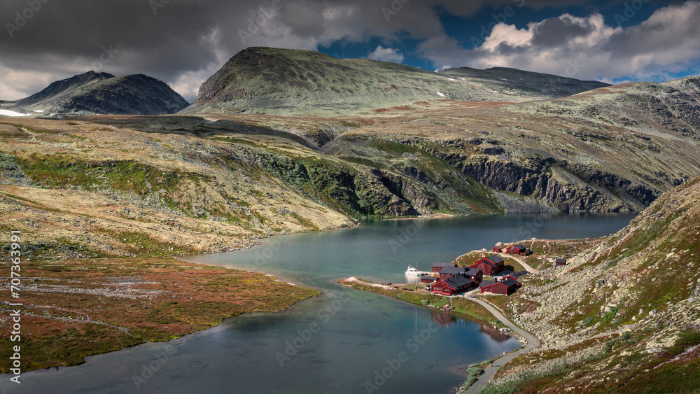 Rondane national park with hut Rondvassbu, blue lake, mountains and cloudy sky.