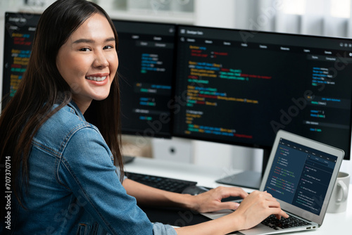 Young Asian in IT developer looking at camera to present with online information on pc with coding program data application  wearing jeans shirt. surround by safety analysis two screens. Stratagem.