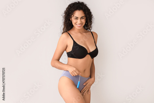 Young African-American woman in menstrual panties with tampon on light background