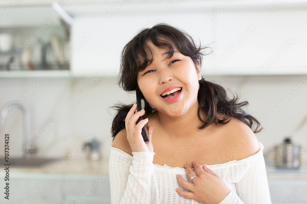 Cheerful girl chatting with friends on the phone in home kitchen