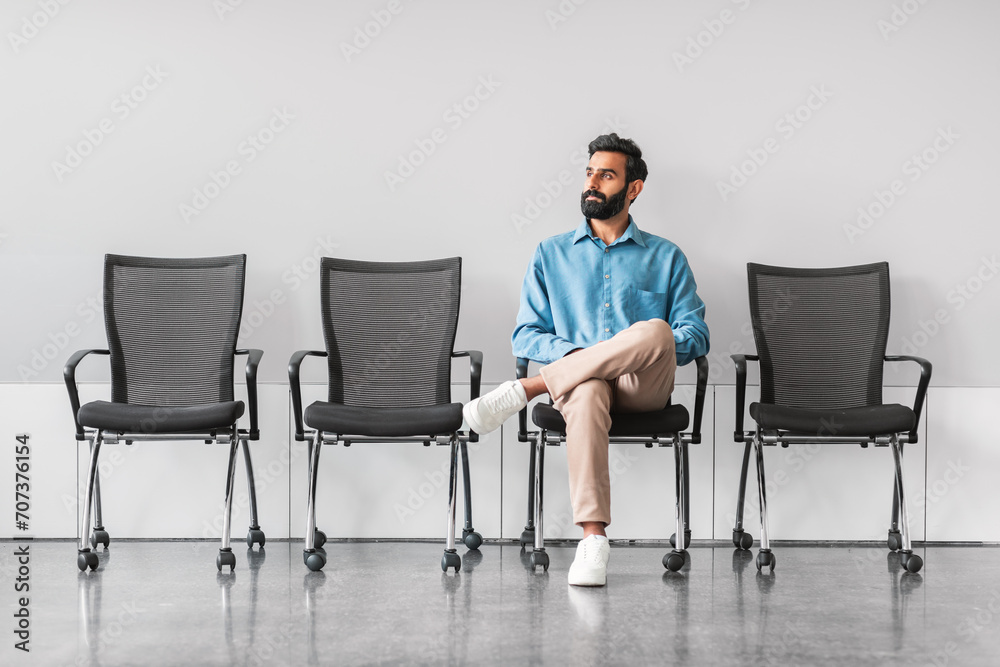 Indian man waiting calmly in office with empty chairs Indian man waiting calmly in office with empty chairs