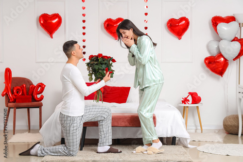 Young man proposing to his girlfriend in festive bedroom. Valentine's Day celebration