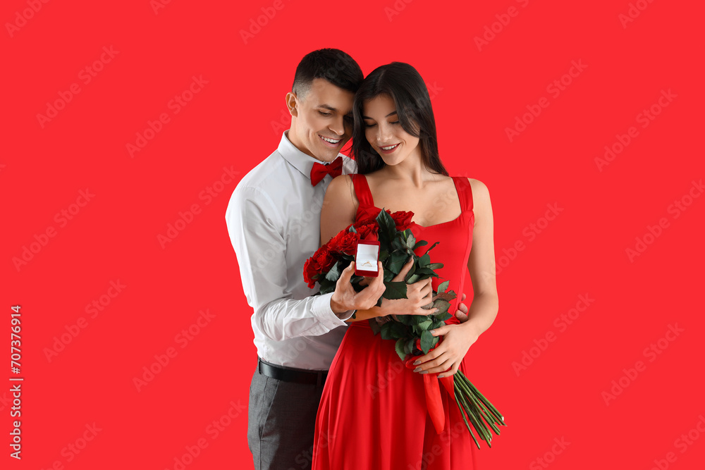 Εκτύπωση καμβά Young engaged couple with wedding ring and bouquet of roses on red background