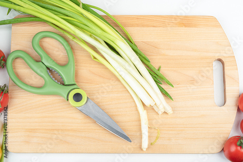 Green onions and kitchen scissors on a wooden cutting board.