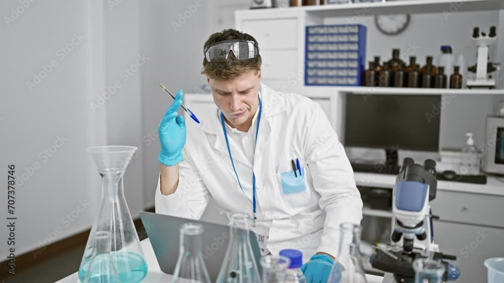 Engrossed in analysis, a handsome young caucasian male scientist, sporting glasses and a beard, probes a doubt while sitting at a laboratory table, passionately engrossed in research on his laptop. Engrossed in analysis, a handsome young caucasian male scientist, sporting glasses and a beard, probes a doubt while sitting at a laboratory table, passionately engrossed in research on his laptop.