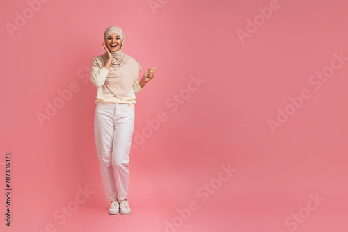 Excited muslim woman in hijab pointing aside at copy space