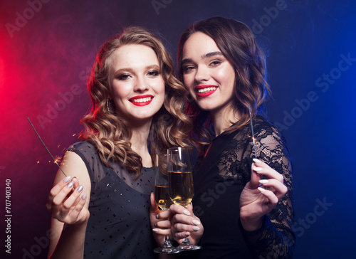 Two charming young women friends with disco balls drinking champagne and having fun together