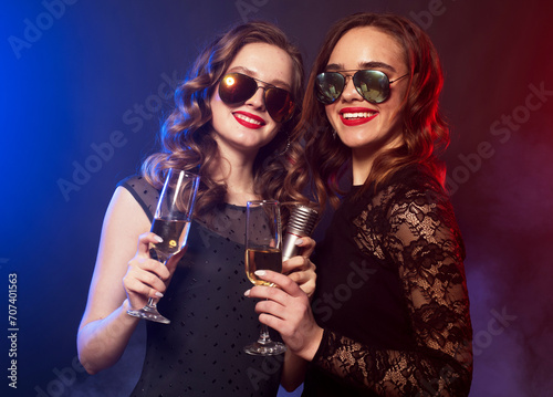 Two charming young women friends with disco balls drinking champagne and having fun together