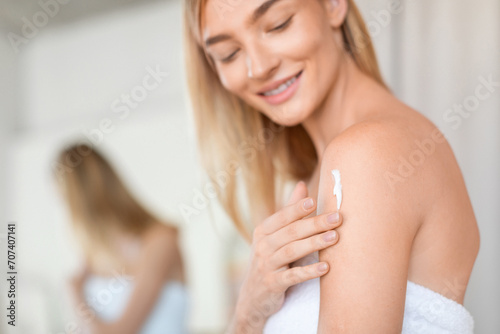 woman wrapped in towel rubs moisturizer on shoulder in bathroom