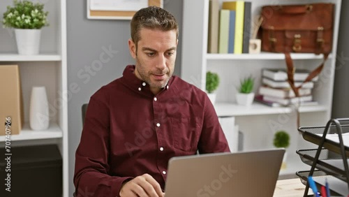 Cheery, confident young hispanic man with tooth-friendly smile, savoring success, happily sitting at the office computer, looking convinced and positive
