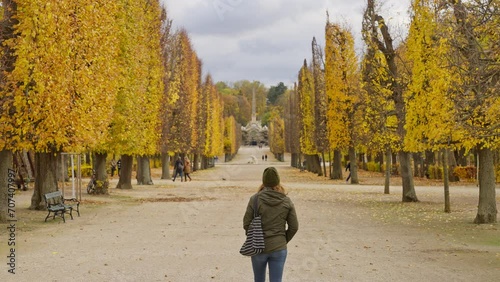 Rear view of woman walking in slow motion down a colorful treelined path during a cold fall