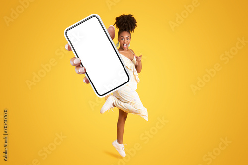 Excited cheerful young african american lady in dress showing phone