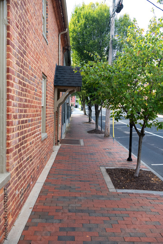 Brick sidewalk along the walls of brick houses. Trees along the road