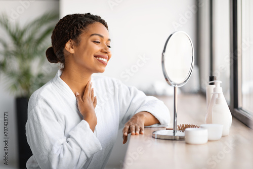 Beautiful black woman looking in mirror and touching neck skin,