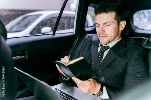 後部座席に乗りながノートパソコンで仕事をする外国人ビジネスマン（白人男性）
 photo