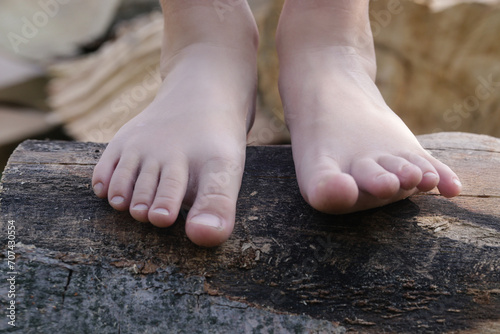Child feet on wood log, barefoot little girl on tree trunk, countryside lifestyle, concept of grounding and connecting with nature