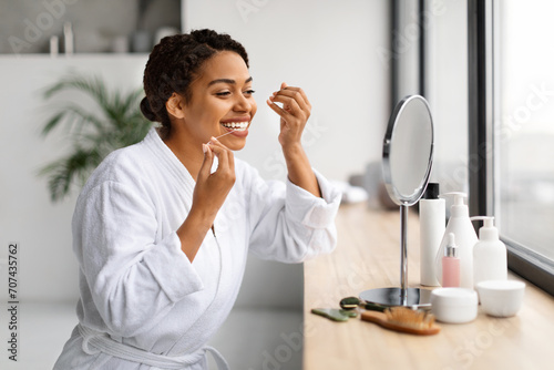 Oral Care. Happy Black Female Looking In Mirror And Using Dental Floss photo