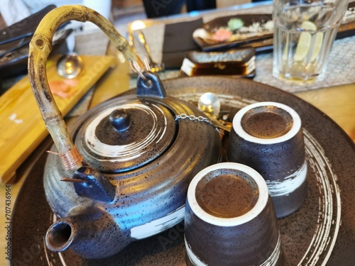 A close-up of an oriental-style brown cutlery set comprising a teapot  two glasses and a tea saucer. 